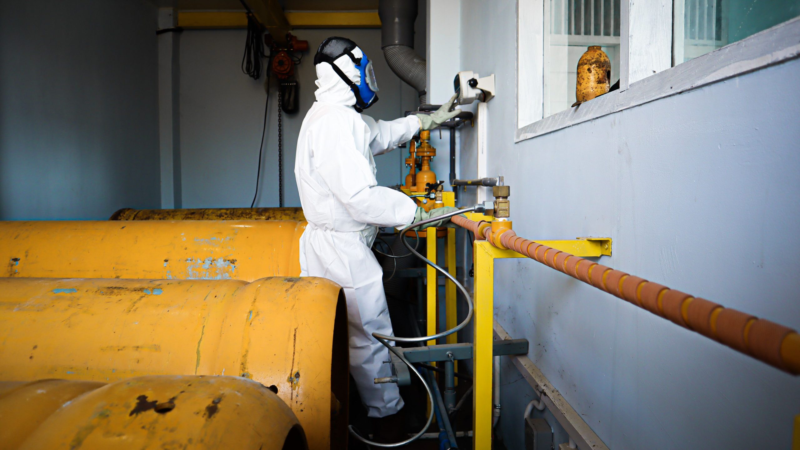 Applications Worker in full protective suit and gas mask handles industrial pipes indoors in Indonesia.